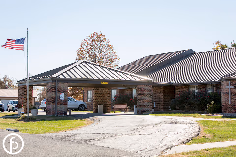 Brick health and rehabilitation building entrance with a covered driveway, American flag, and parked cars.