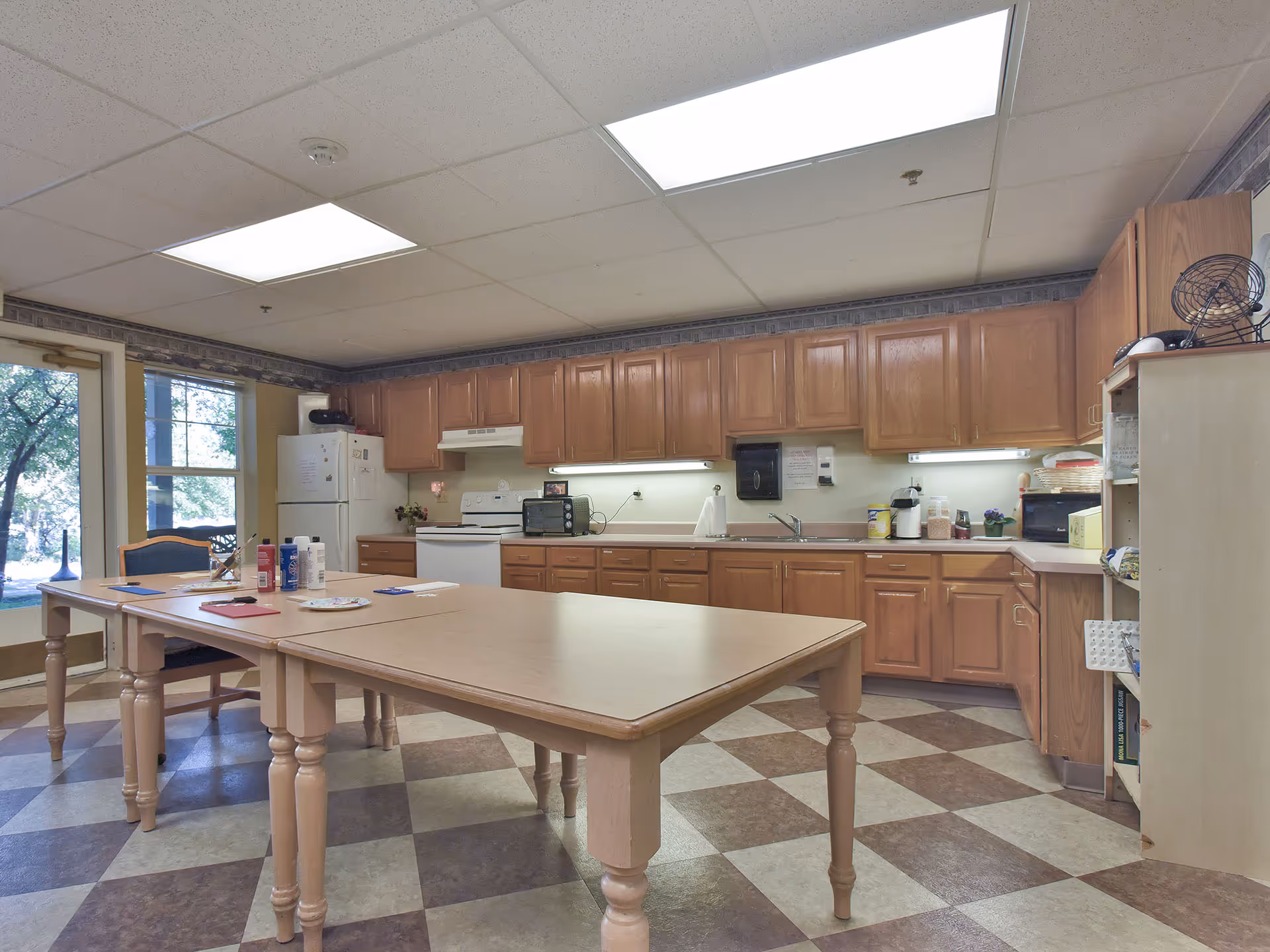 Communal kitchen and activity area with a long table, wooden cabinets, refrigerator, stove, and sink.