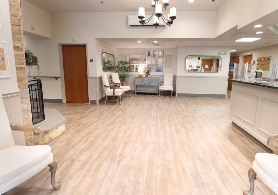 Bright senior living facility lobby with wood-look flooring, seating, and a reception desk.
