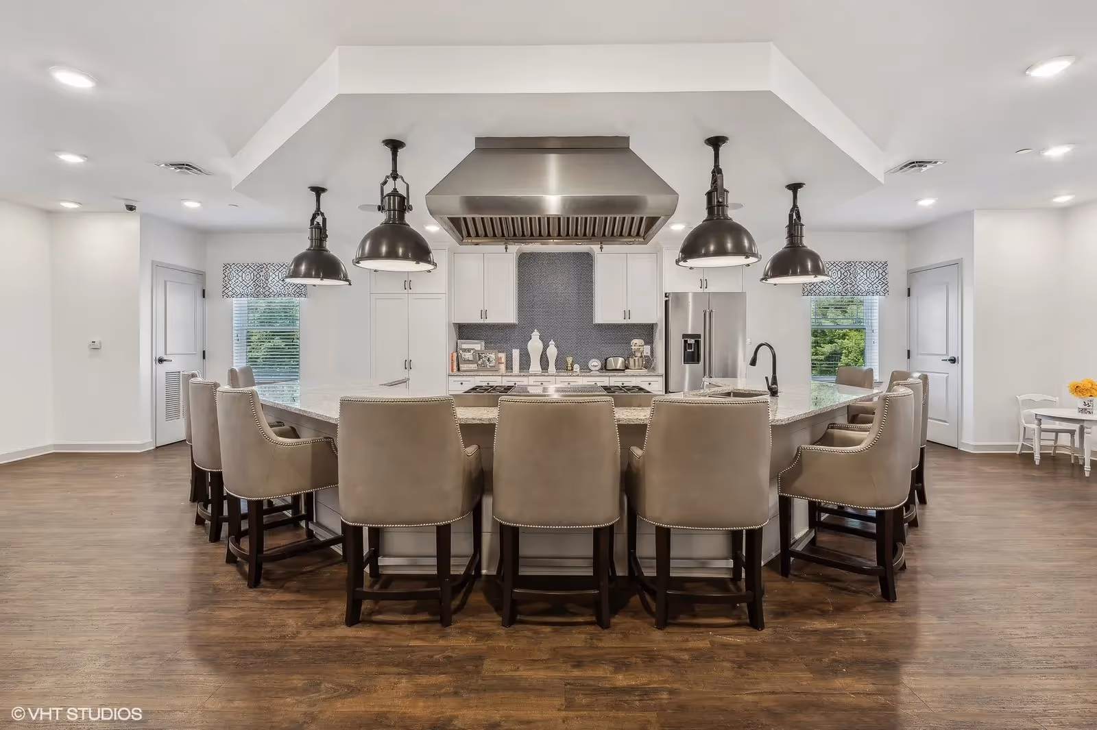 Spacious modern kitchen with a large central island surrounded by upholstered bar stools, pendant lights, and stainless steel appliances.