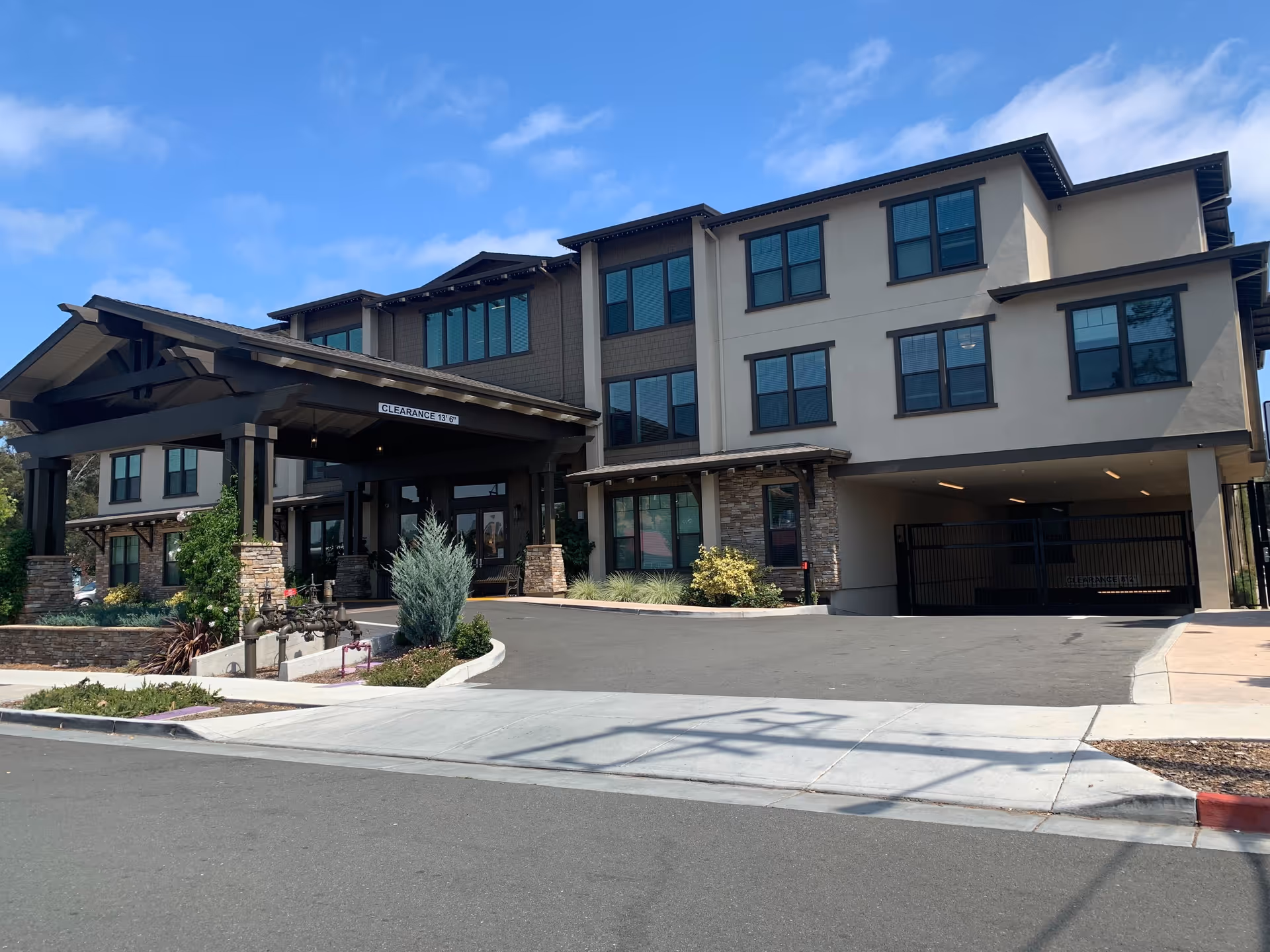 Exterior front view of a three-story senior living facility named The Vincent, featuring a covered entrance with stone pillars, multiple windows, and a driveway leading to an underground parking garage.