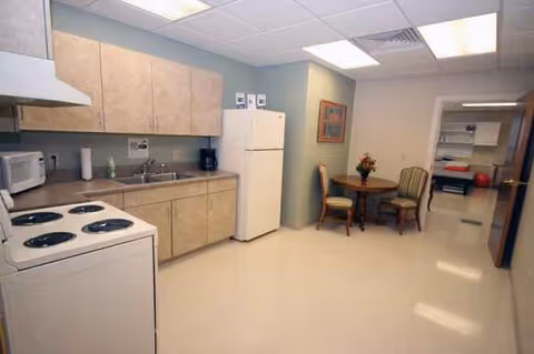 A compact kitchen in a senior living facility with stove, fridge, and a small table.