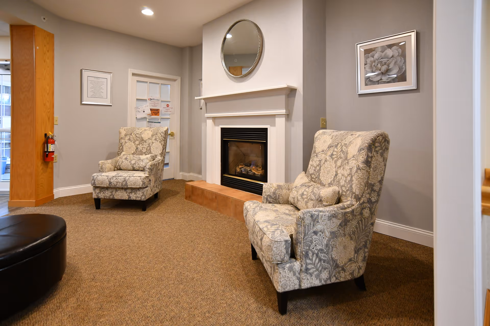 Cozy seating area with two patterned armchairs flanking a fireplace with a round mirror above it.