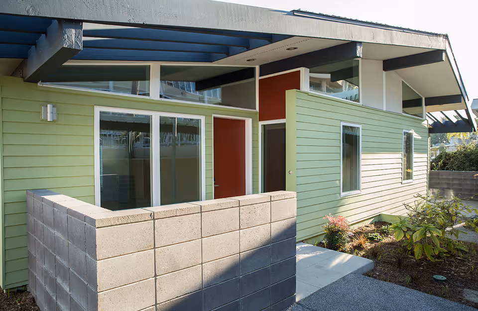 Modern single-story building exterior with green siding, red doors, and a small concrete block patio wall.