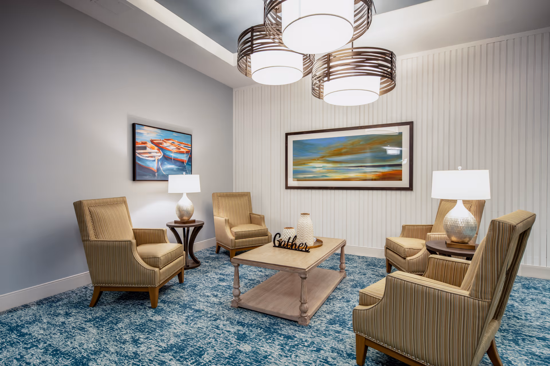 A cozy seating area with four upholstered armchairs around a wooden coffee table, decorative lamps, artwork, and pendant lights.