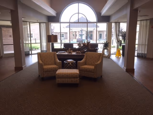 Lobby seating area with two upholstered armchairs, an ottoman, a side table and a large arched window overlooking a courtyard fountain.
