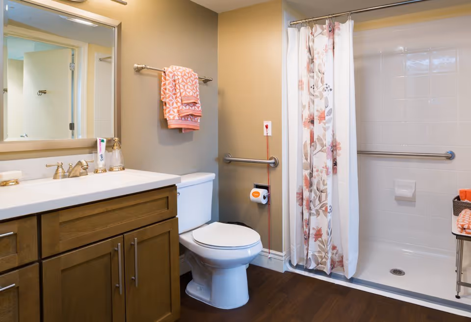 Bright accessible bathroom with a vanity, toilet, grab bars, and a shower with a floral curtain.