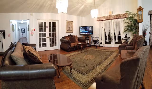 Spacious living room with multiple sofas and armchairs arranged around a large rug, coffee table, TV, and French doors.