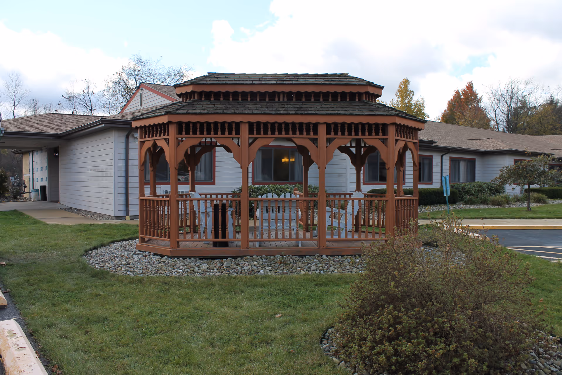 A wooden gazebo sits on a landscaped lawn in front of a single-story healthcare building.