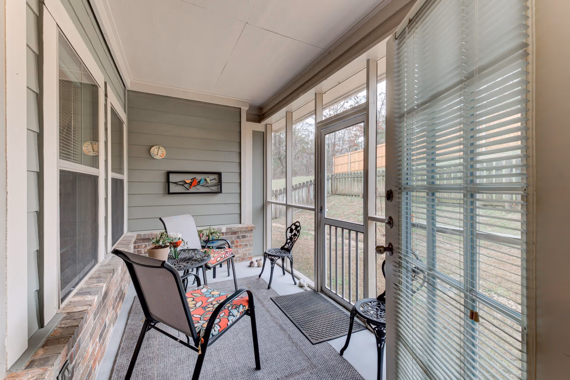 Screened porch with seating, a small table, and a view of a fenced backyard.