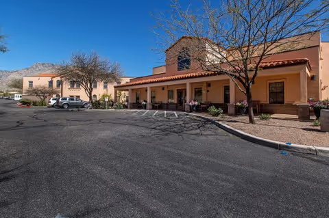 Exterior view of Tucson Place at Ventana Canyon with parked cars and a tan stucco building.