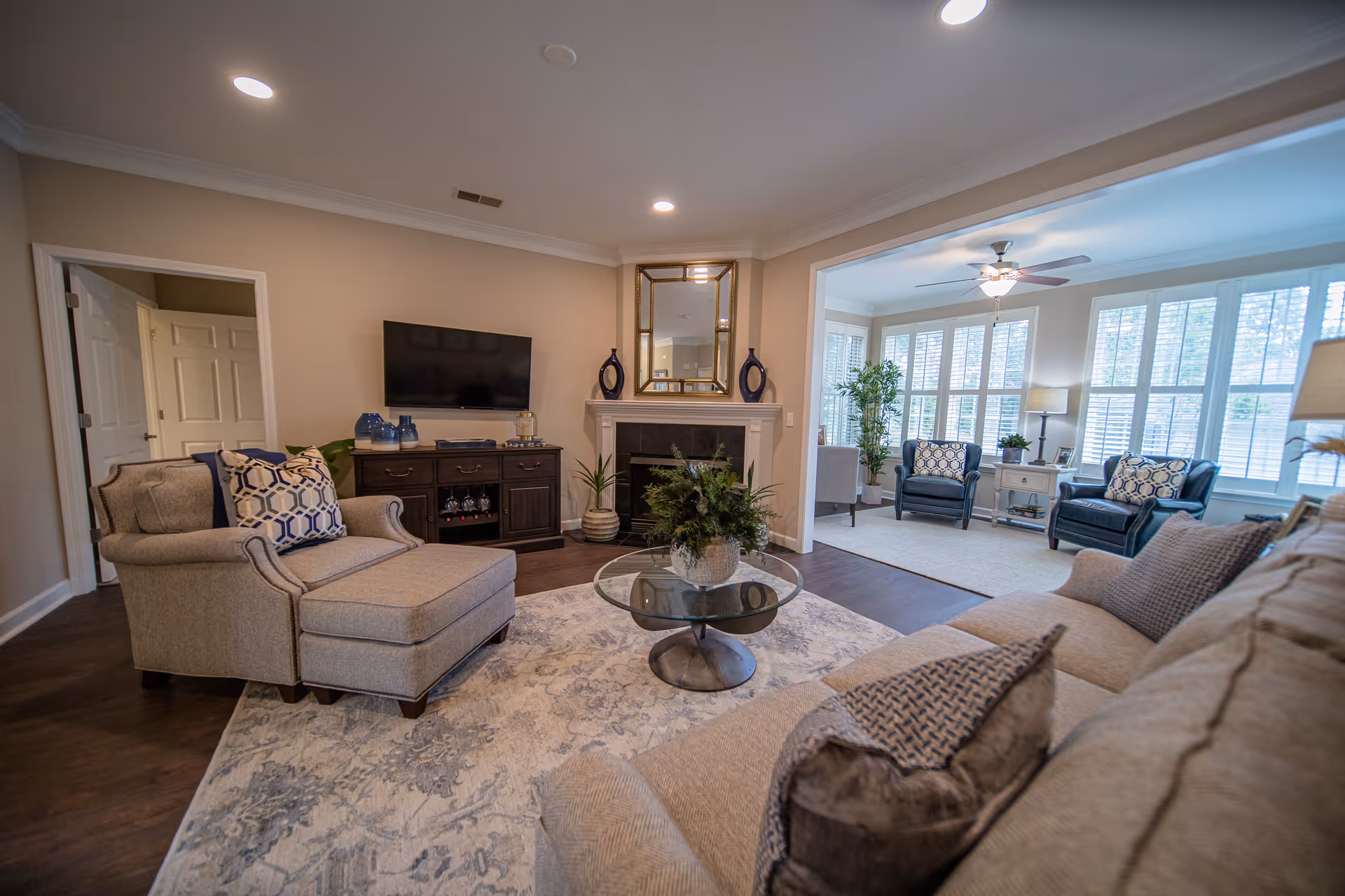 Spacious furnished living room with sofa, armchairs, coffee table, fireplace and TV opening into a bright sunroom.