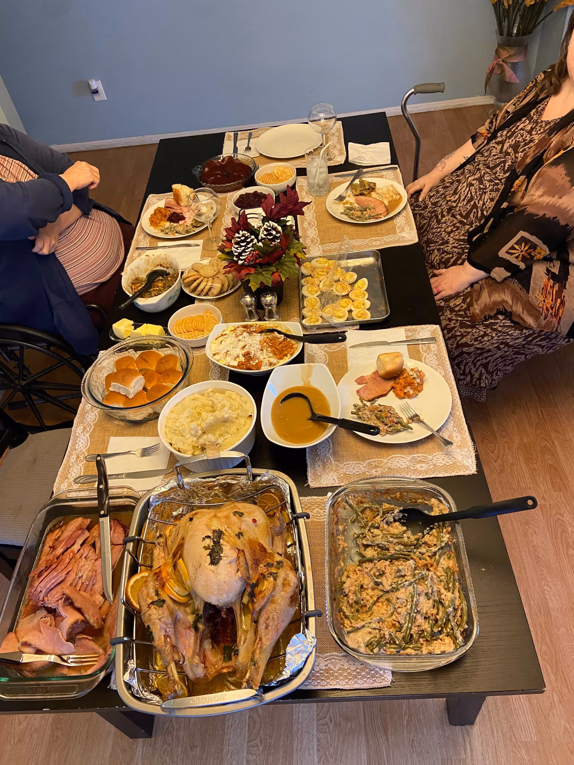 Overhead view of a dining table set with a roast turkey, ham, side dishes and two seated people at a holiday meal.
