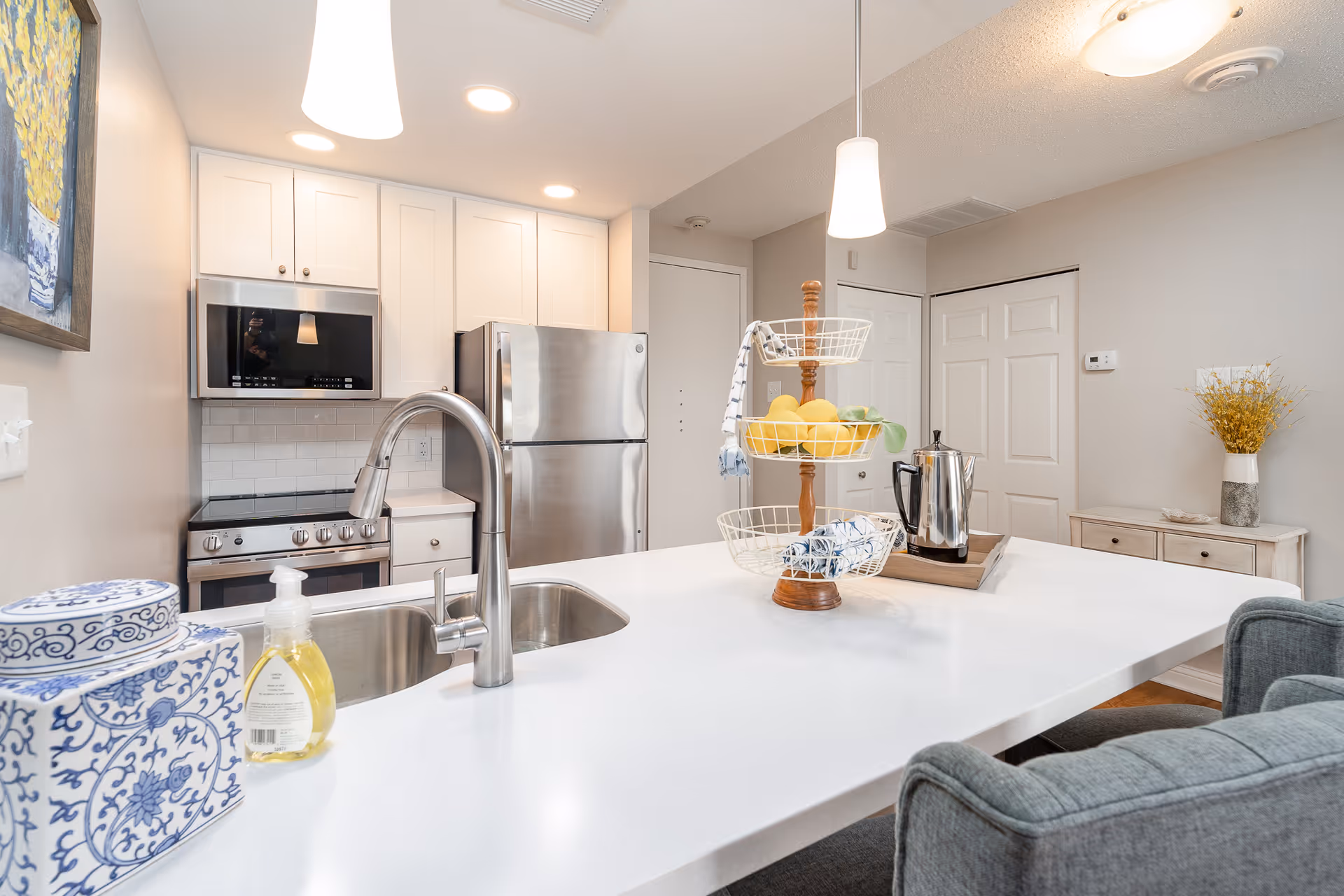 Bright modern kitchen with a white island, stainless steel appliances, sink, and a tiered fruit basket on the counter.