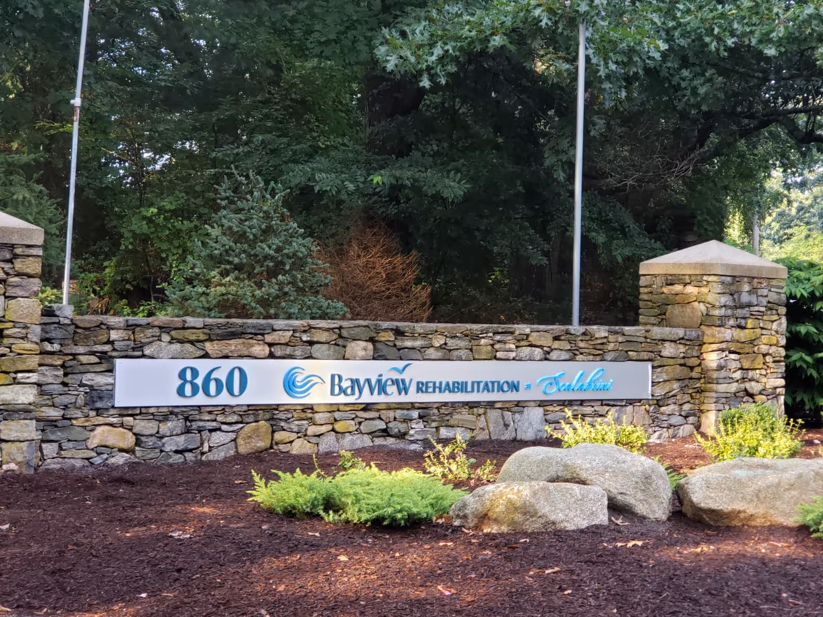 Stone wall entrance sign for Bayview Rehabilitation at Scalabrini with the number 860, surrounded by greenery and trees in the background.