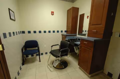 Interior grooming area with barber chair, mirrors, and wooden cabinets in a senior facility.