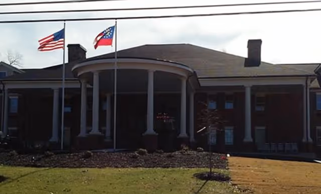 Front entrance of a brick building with a circular columned portico, two flagpoles, and a small lawn.