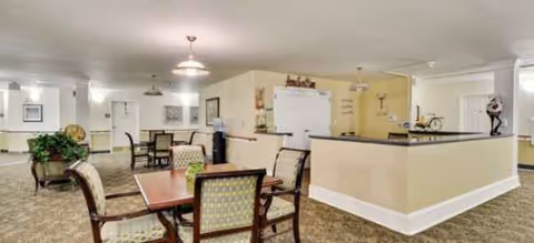 Interior dining area with wooden tables, upholstered chairs, soft lighting, and a service counter.