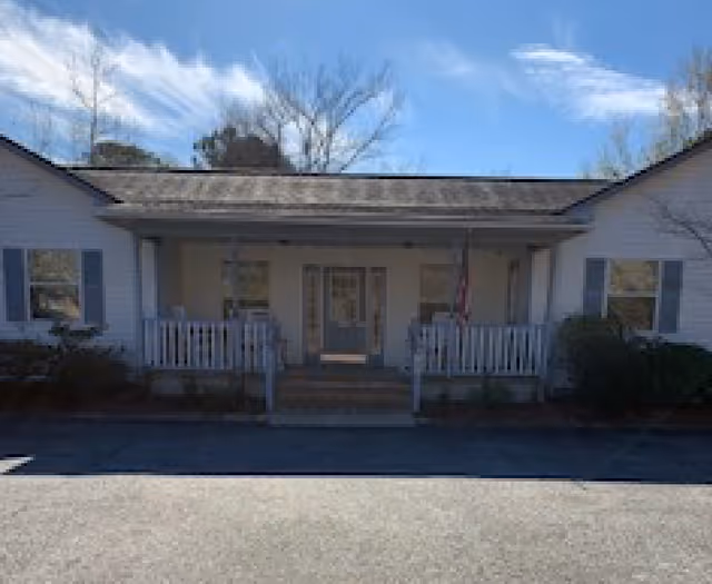Single-story white residential building with a covered front porch, railing, and an American flag.