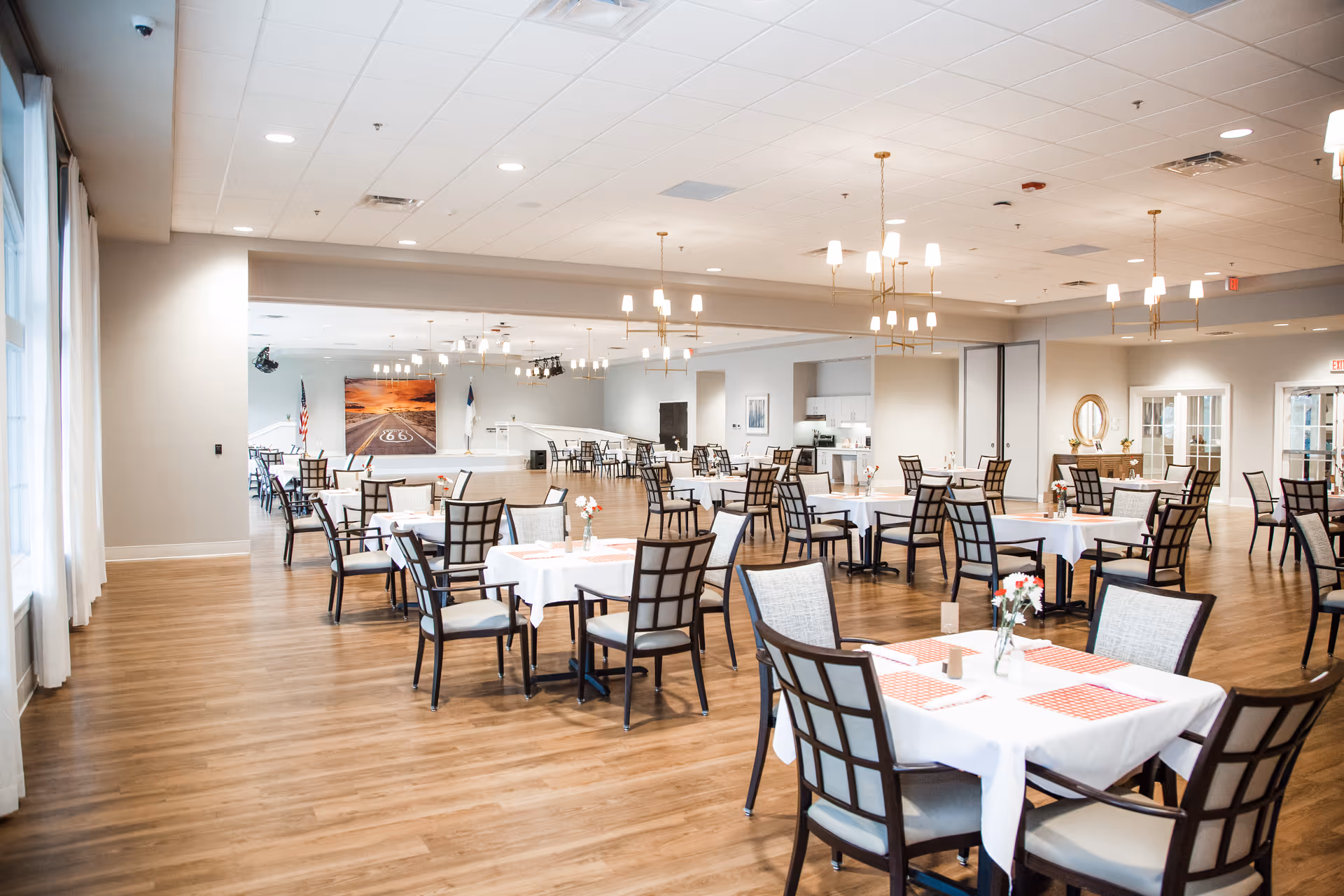 Spacious dining room with multiple set tables and chairs, wood floors, and hanging chandeliers.