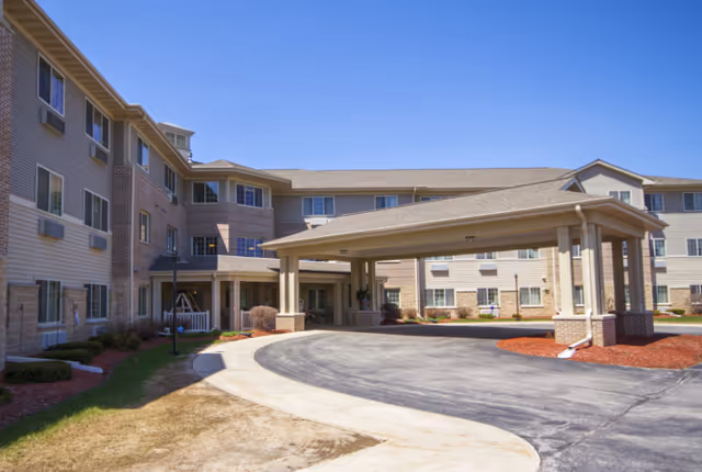 Exterior front of a multi-story senior living facility featuring a covered porte-cochère entrance and circular driveway.
