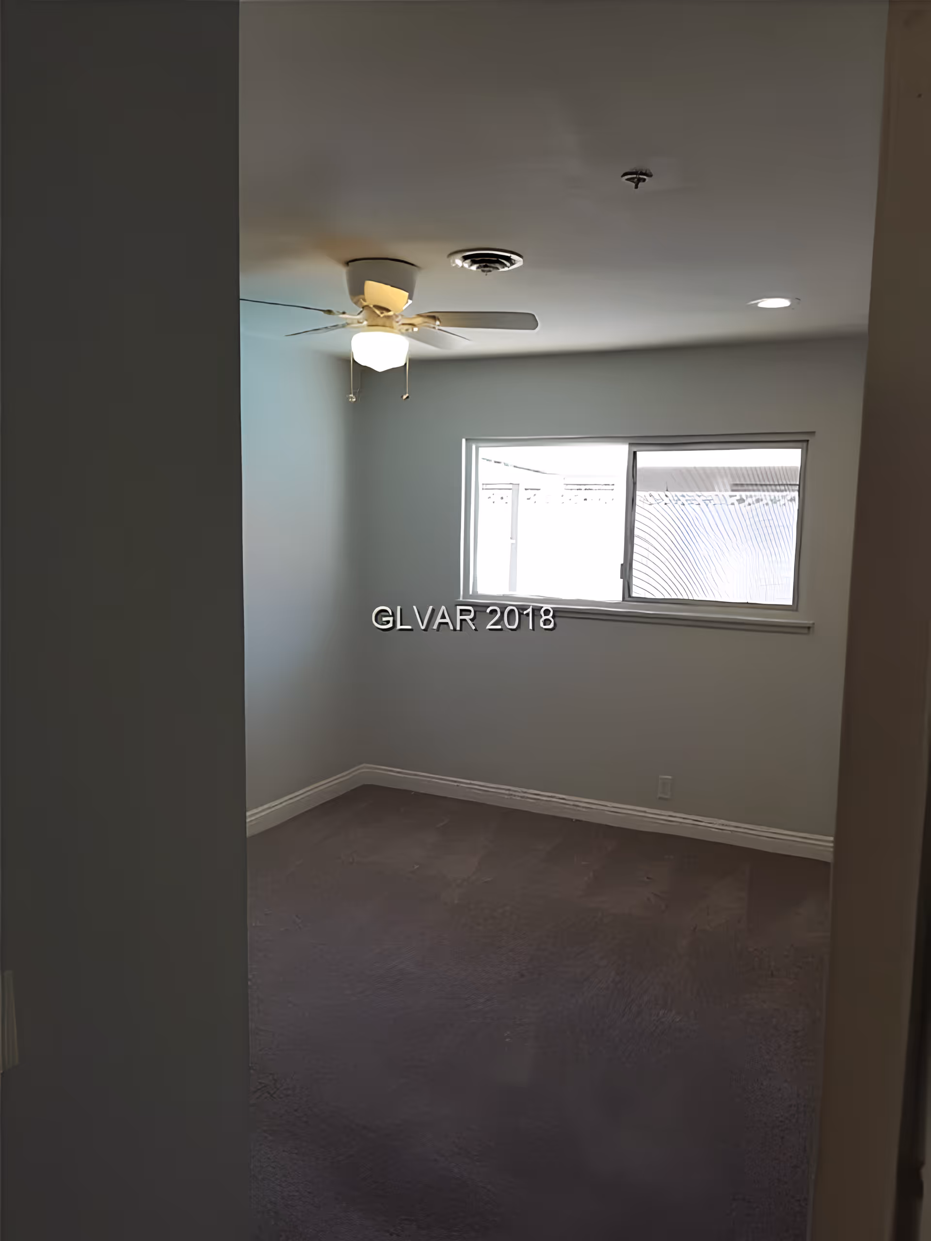 Empty room with gray carpet, white walls, a ceiling fan with light, and a window letting in natural light.