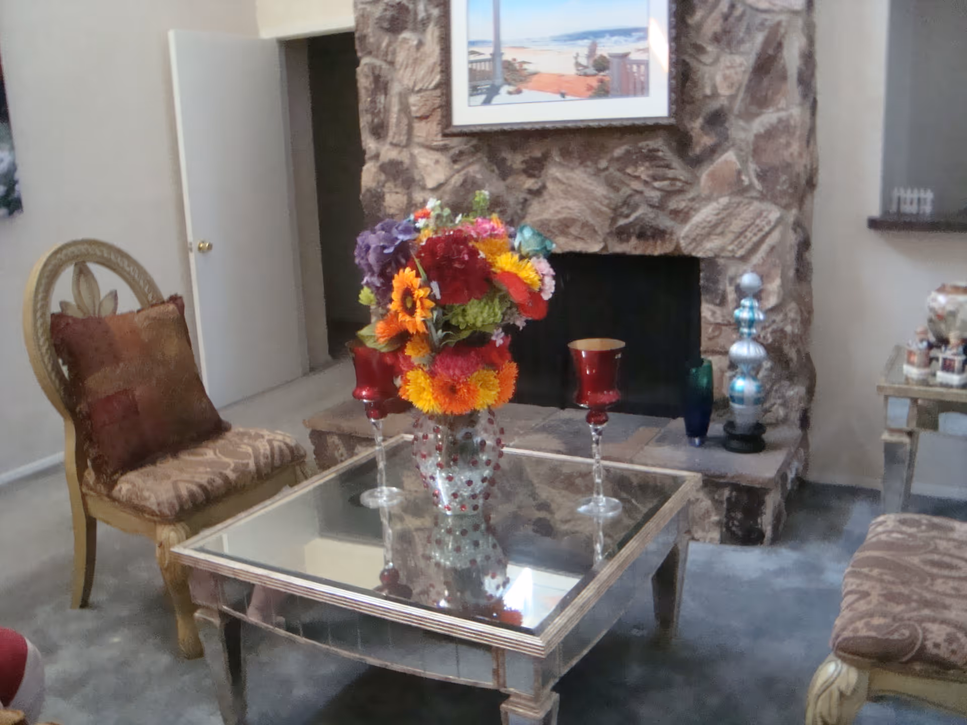 A cozy living room with a glass-topped coffee table holding a colorful floral arrangement in front of a stone fireplace.