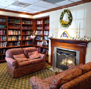Cozy lounge with red upholstered chairs, bookshelves, and a lit fireplace.