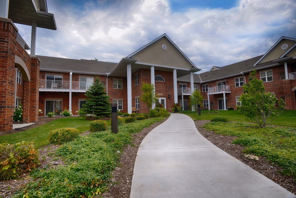 Brick two-story senior apartment building with a covered central entrance and a curved walkway through landscaped grounds.