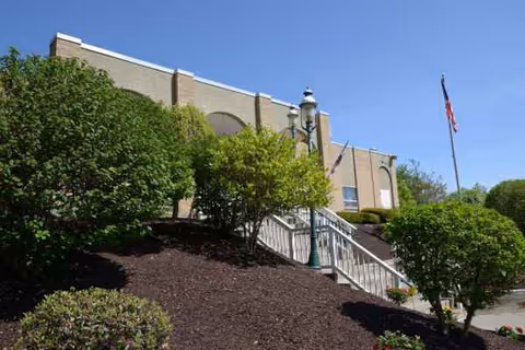 Front view of Absolut Center for Rehabilitation and Nursing building with stairs, landscaping, and American flag.