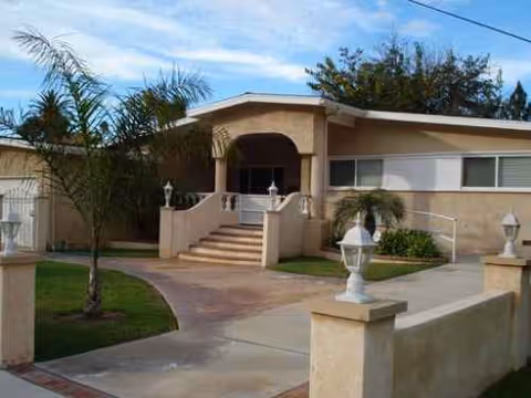 Single-story beige senior living home with steps, arched entrance, and palm trees.