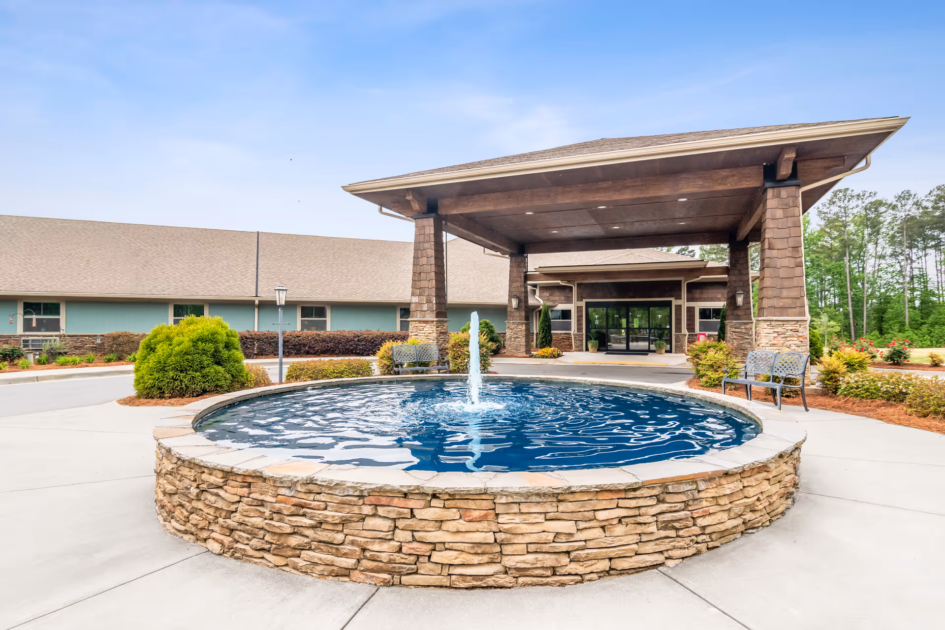 Circular stone fountain in front of Oaks at Hampton entrance with a covered porte-cochère
