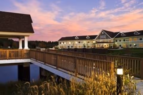 Wooden walkway leading to an illuminated residential building at sunset with landscaped grounds.