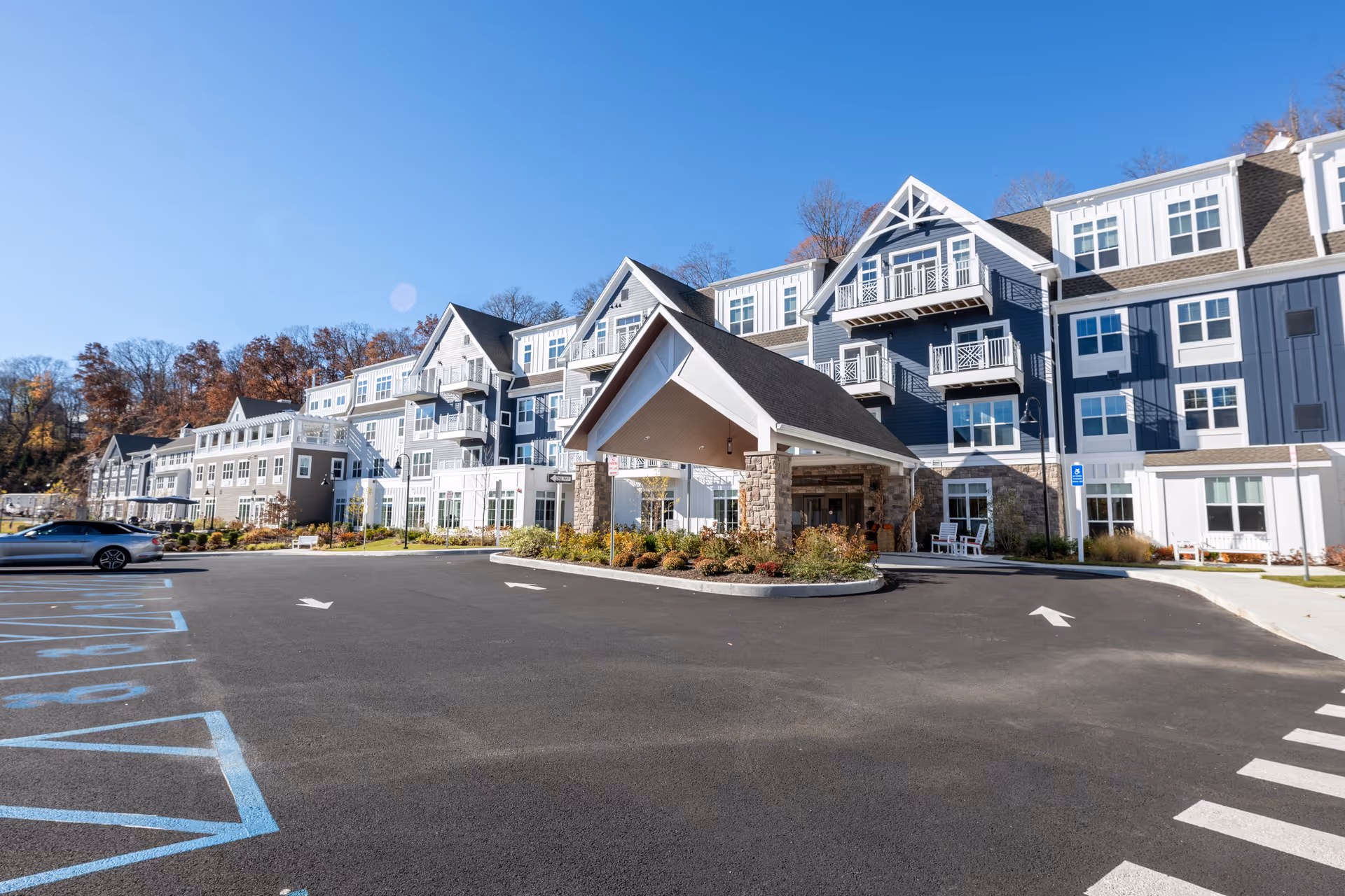 Front entrance and porte-cochere of a multi-story senior living building with a parking lot under a clear blue sky.