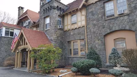 Stone-clad senior living facility exterior with arched entry, turret, and landscaped front yard.
