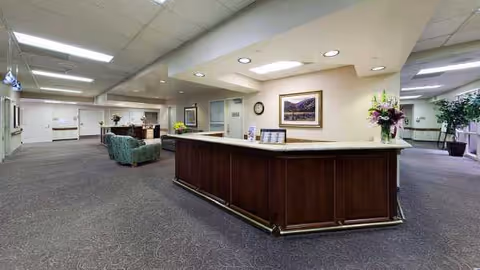 Spacious lobby with curved reception desk, seating area, plants, and framed artwork.