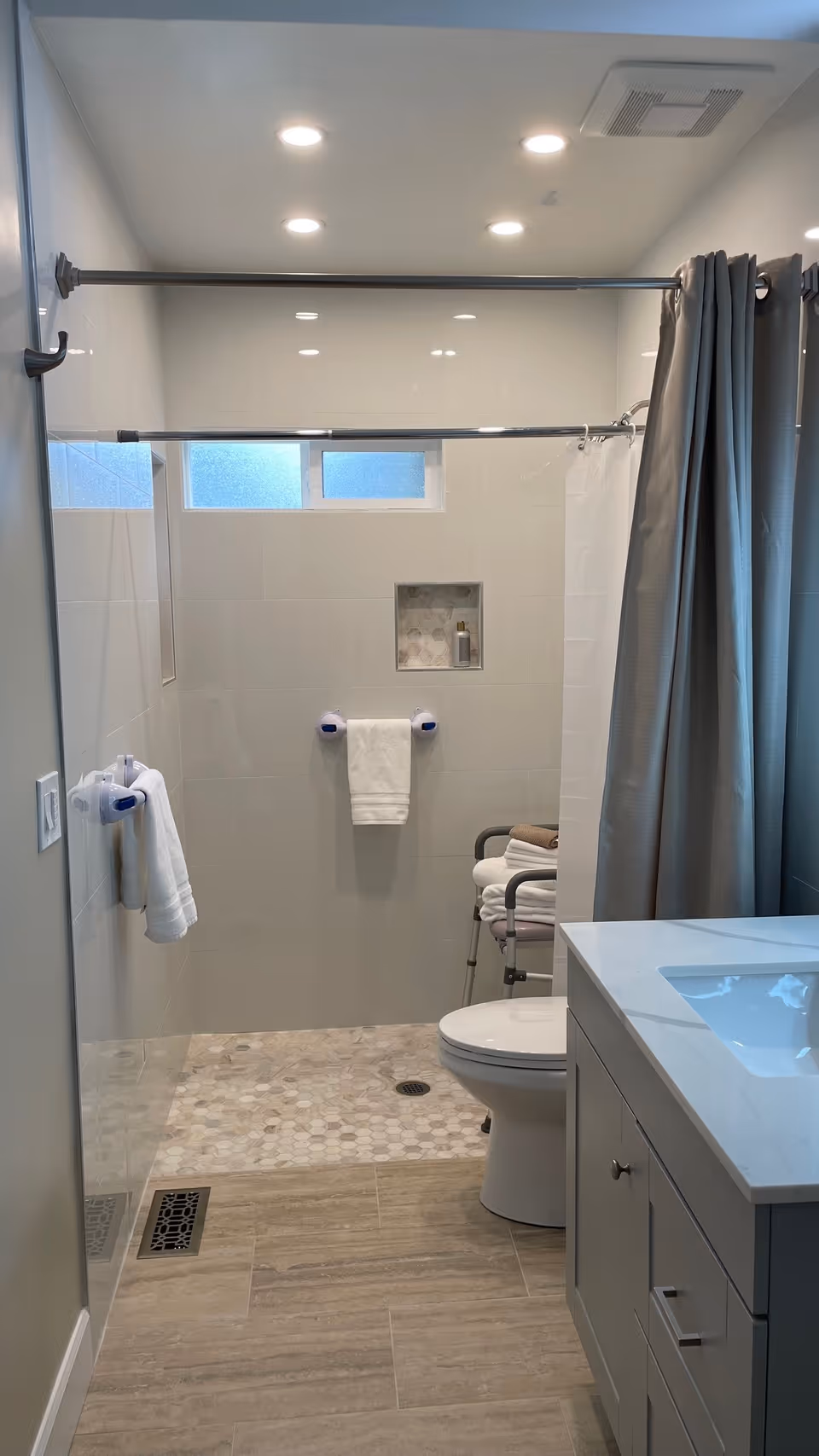 Bright modern bathroom with a walk-in shower (curtain and bench), toilet, vanity with sink, and neatly folded towels.