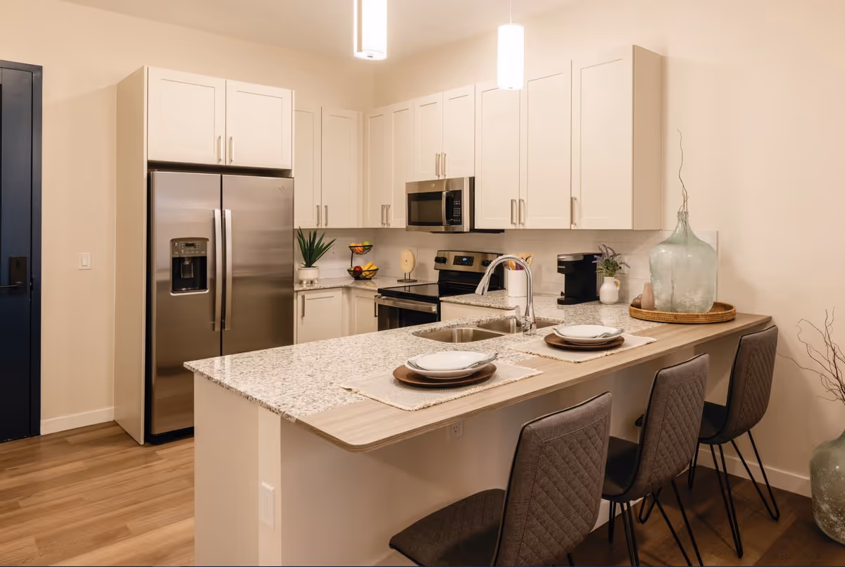 Modern open kitchen with white cabinets, stainless steel appliances, and a breakfast bar with three stools.