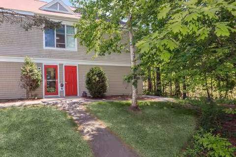 Front exterior of a beige senior living building with red doors and trees.