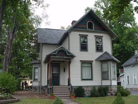 A two-story house-style senior living facility with a porch and green lawn.