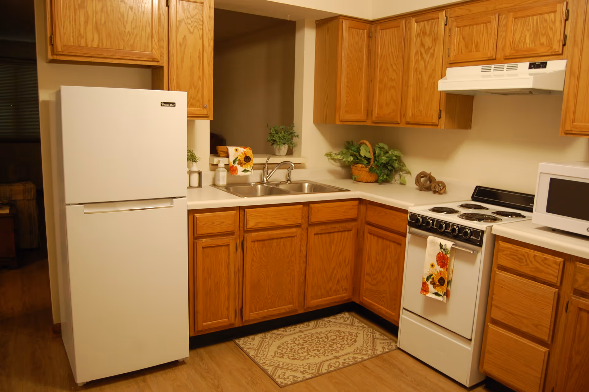 Cozy kitchen with oak cabinets, a white refrigerator and stove, a double sink, and a microwave on the countertop.