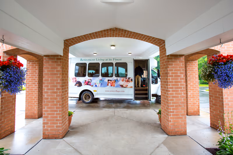 A shuttle bus parked under a brick-covered porte-cochere entrance with hanging flower baskets.