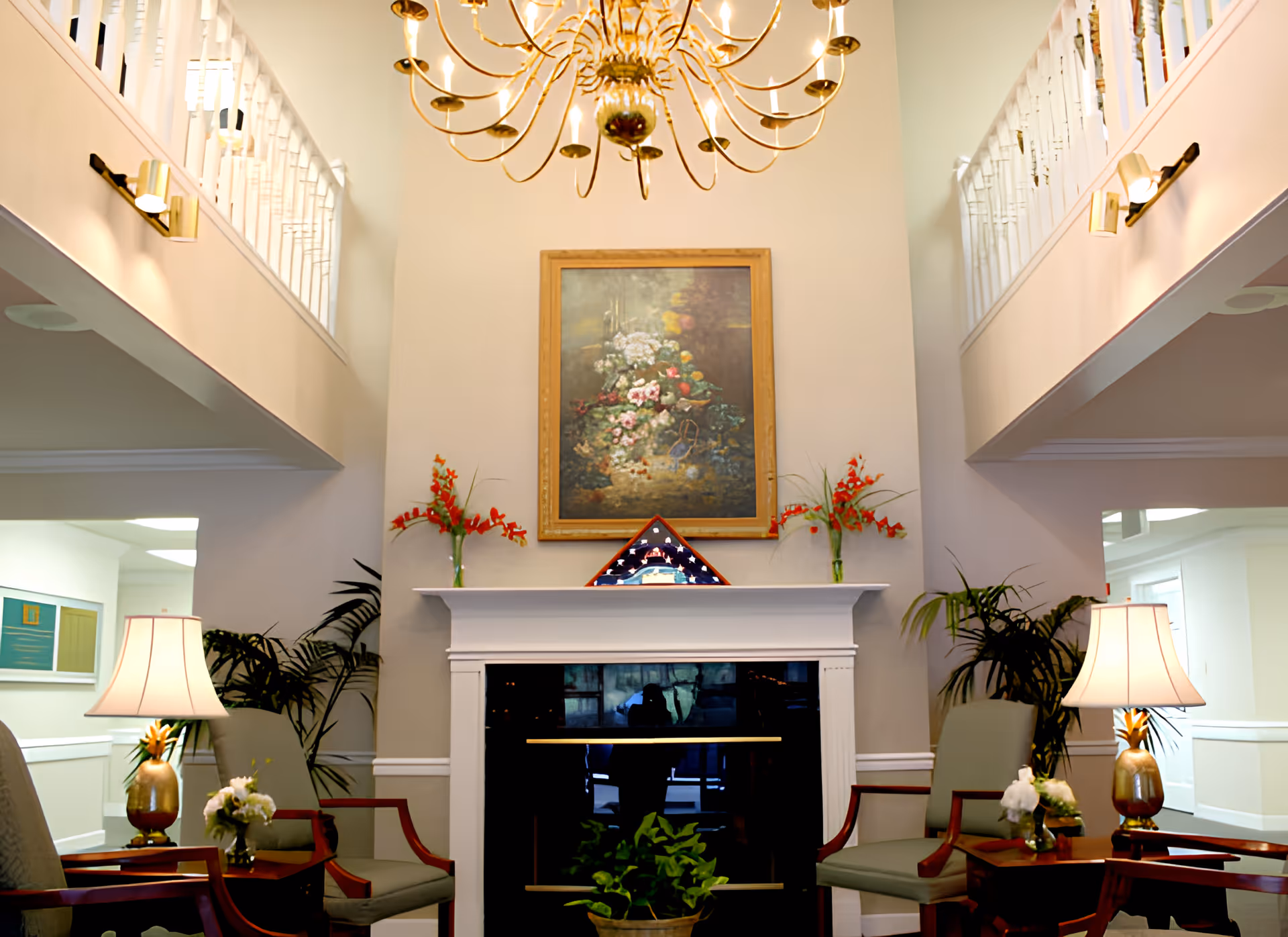 Bright two-story common room with a fireplace, seating, plants, and a chandelier.