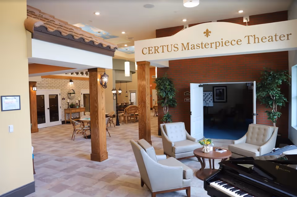 Interior common area of a memory care facility with seating, a piano, and a sign reading 'CERTUS Masterpiece Theater'.