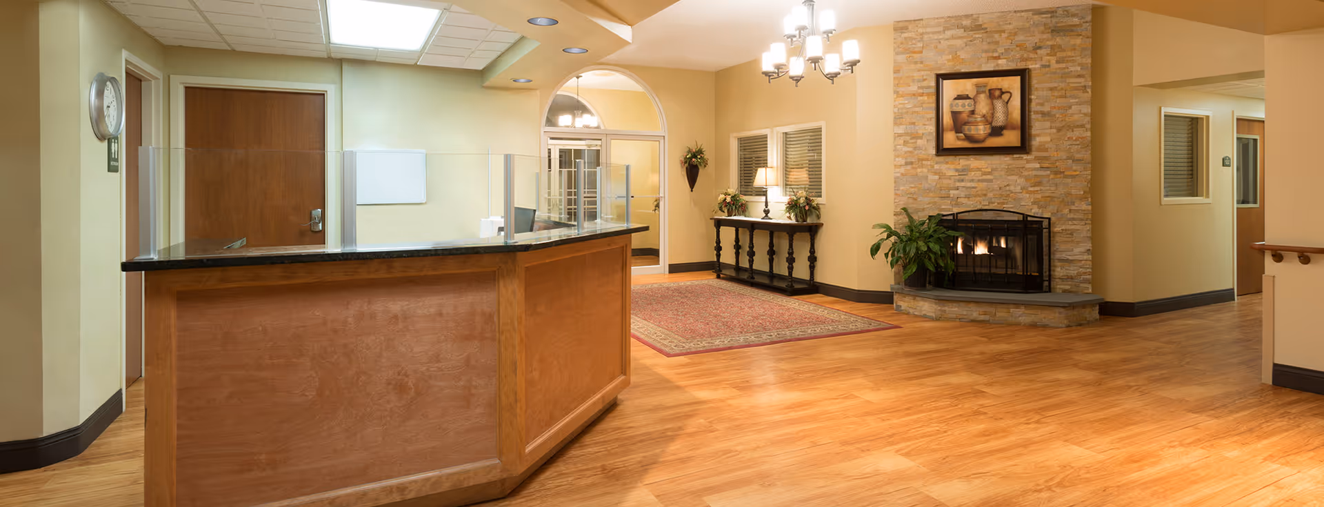 Reception desk in a warm lobby with a fireplace, console table, chandelier, and hardwood floors.
