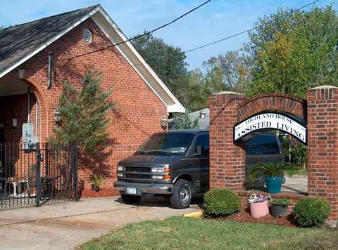 Brick assisted living facility front entrance with sign, archway, and parked van.