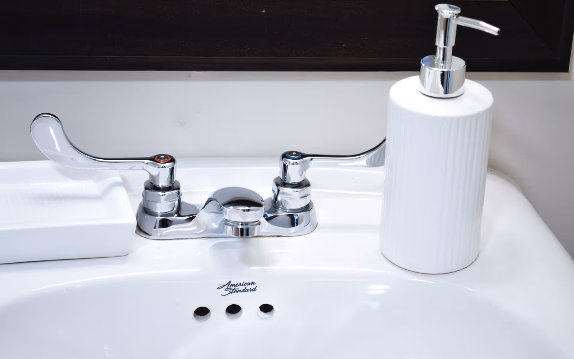 Close-up of a white bathroom sink with a chrome faucet and a white soap dispenser.