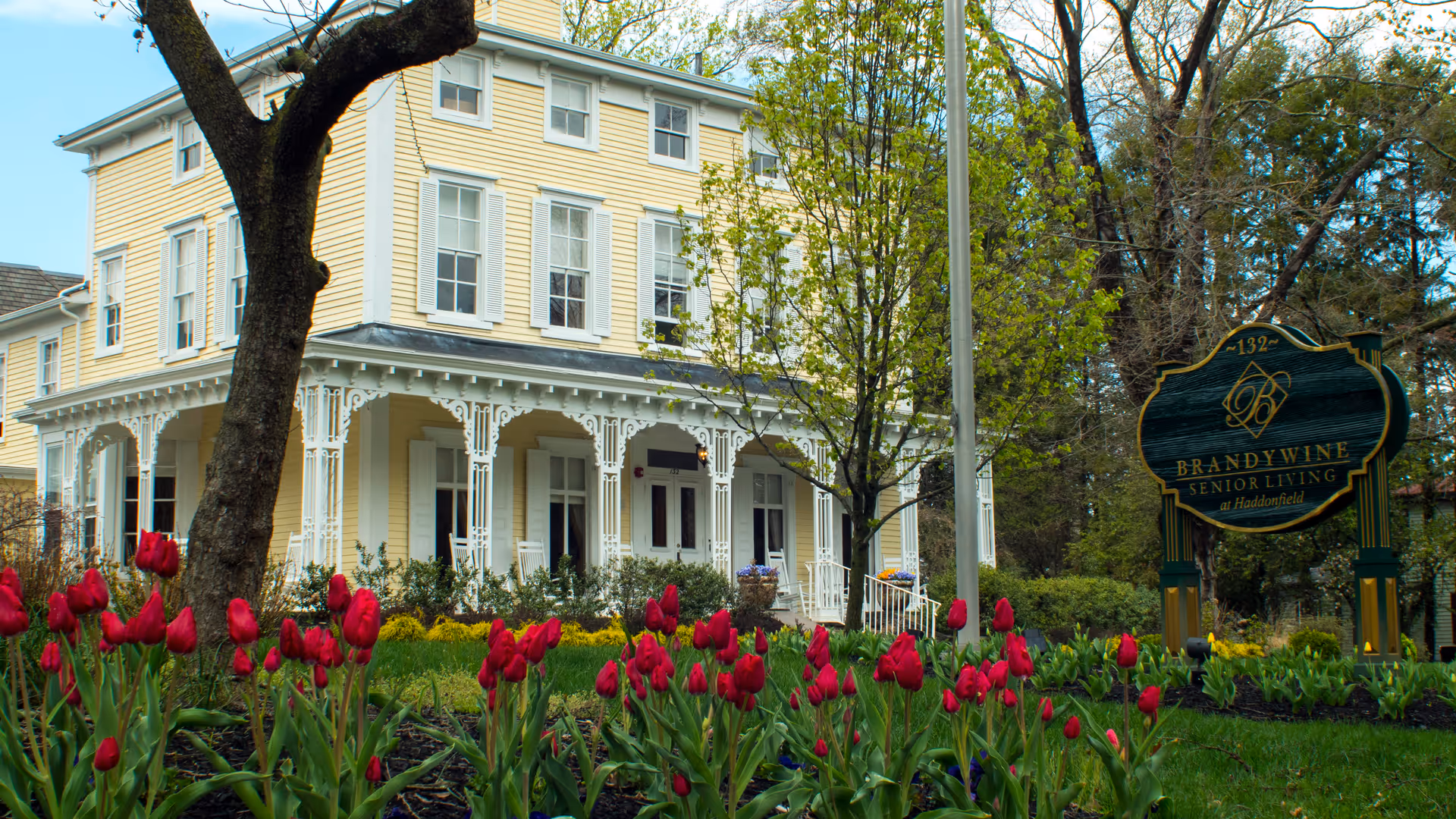 Yellow two-story senior living building with a white porch and bright red tulips in foreground.