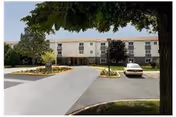 Front view of Creekwood senior living building with driveway, cars, and trees.