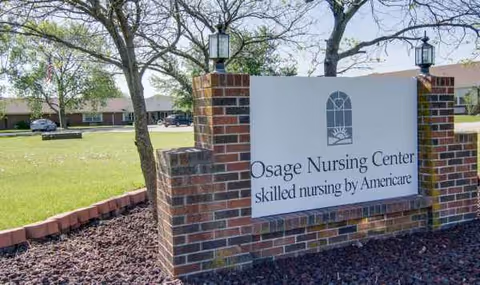 A brick Osage Nursing Center sign sits on a brick pedestal beside trees and grass.